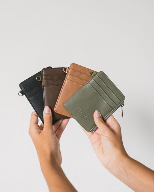 A womans hands, holding four colorways of the RFID Lauren Wallets from Pink Cove, against a white background.