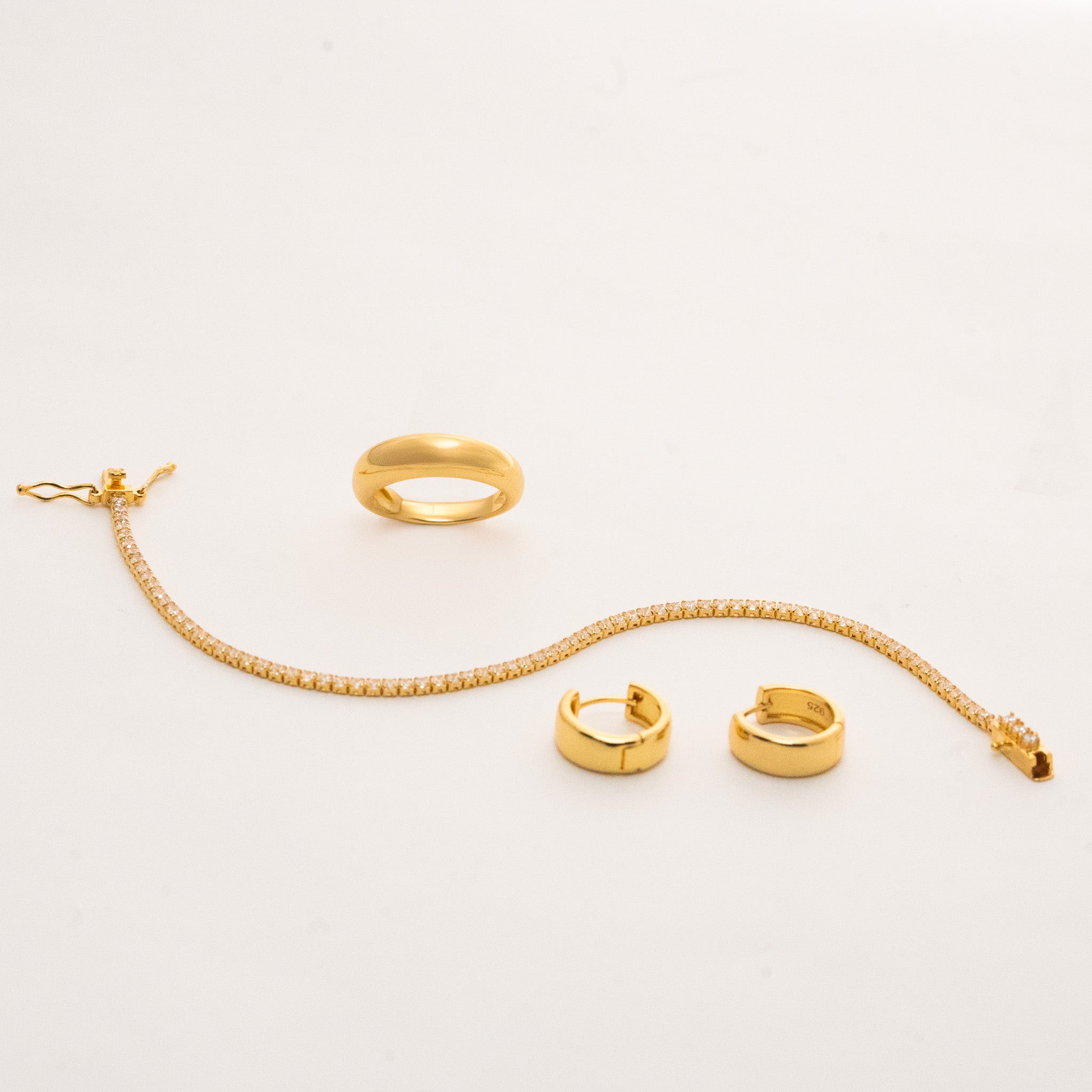 Gold jewelry set from Pink Cove featuring a simple bracelet, a simple ring, and a pair of huggie earrings.