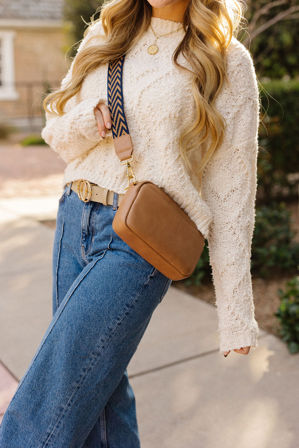 Woman modeling a brown leather bag with a navy and alone cheveron strap from Pink Cove with a white sweater and jeans.