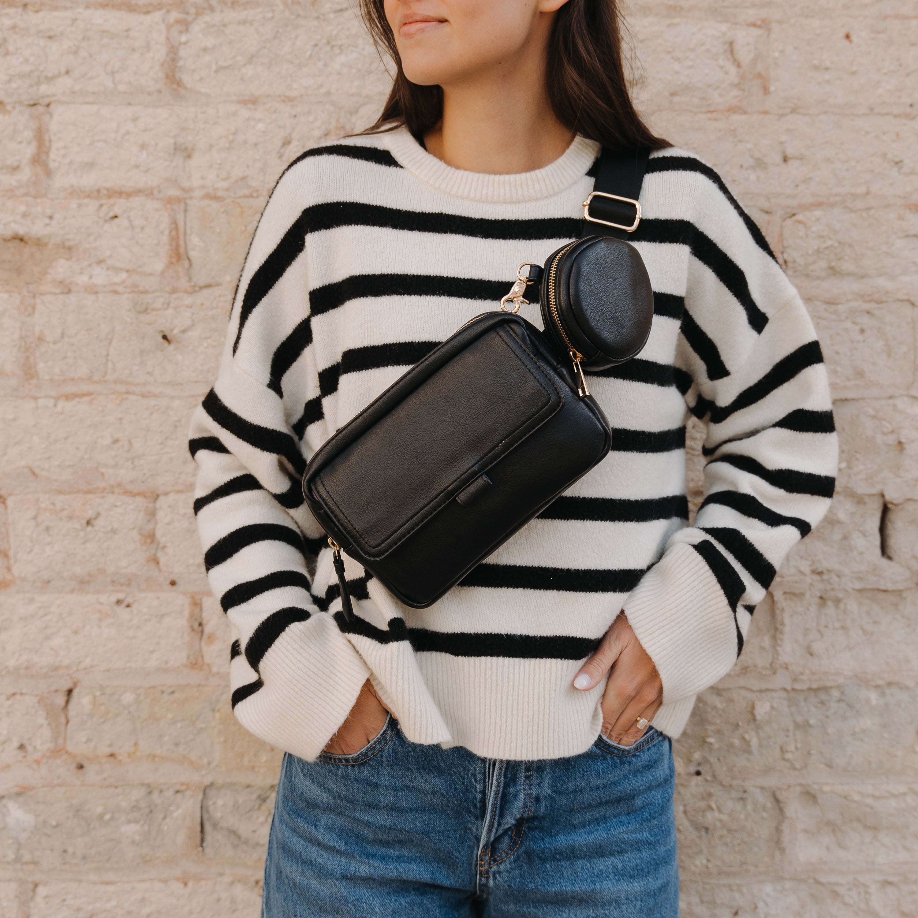 Woman modeling a black leather Charlie Belt bag from Pink Cove in front of a white brick wall.