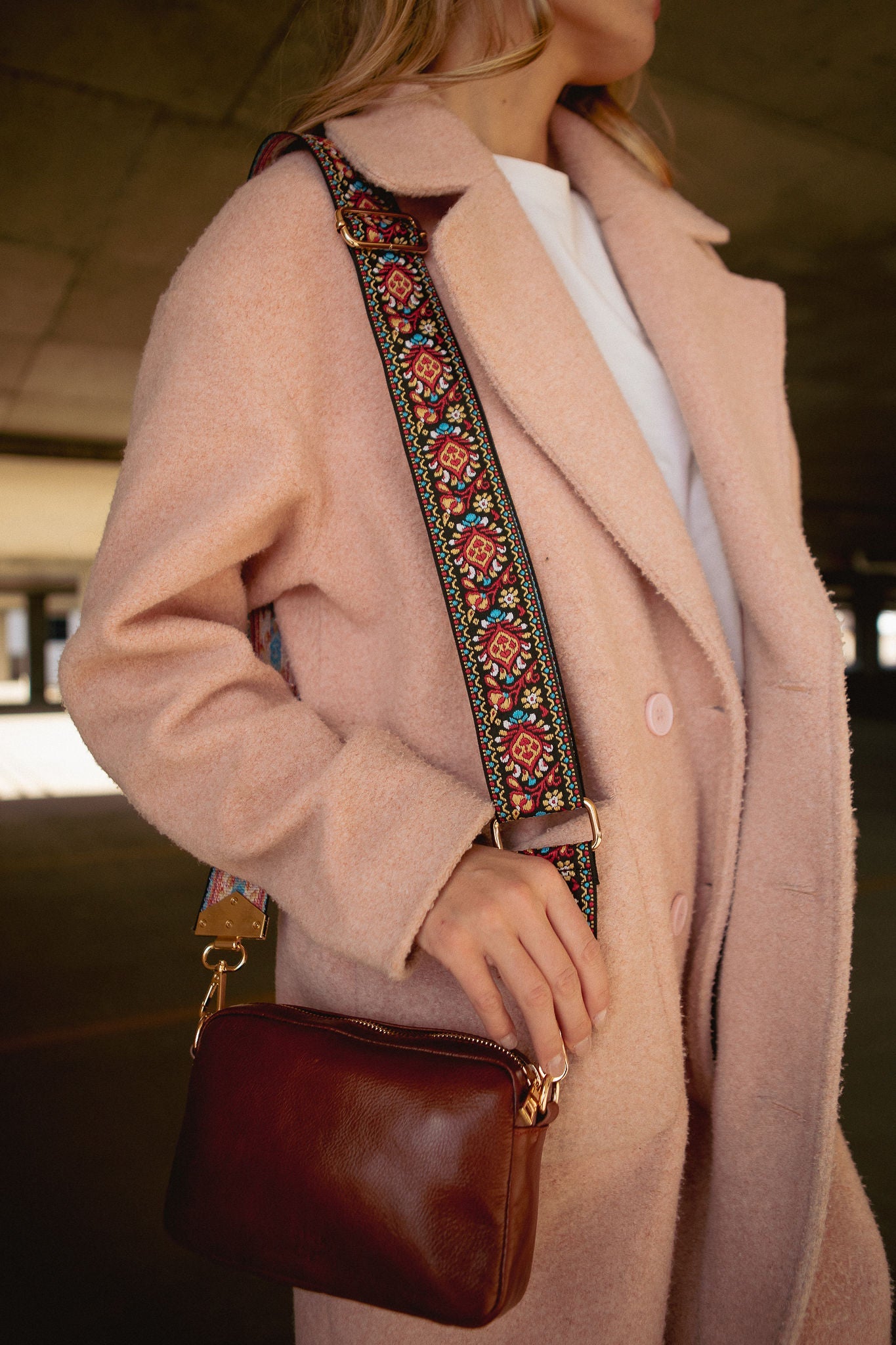 Woman modeling a dark brown leather cross body bag with a colorful strap from Pink Cove, wearing a pink trench coat.