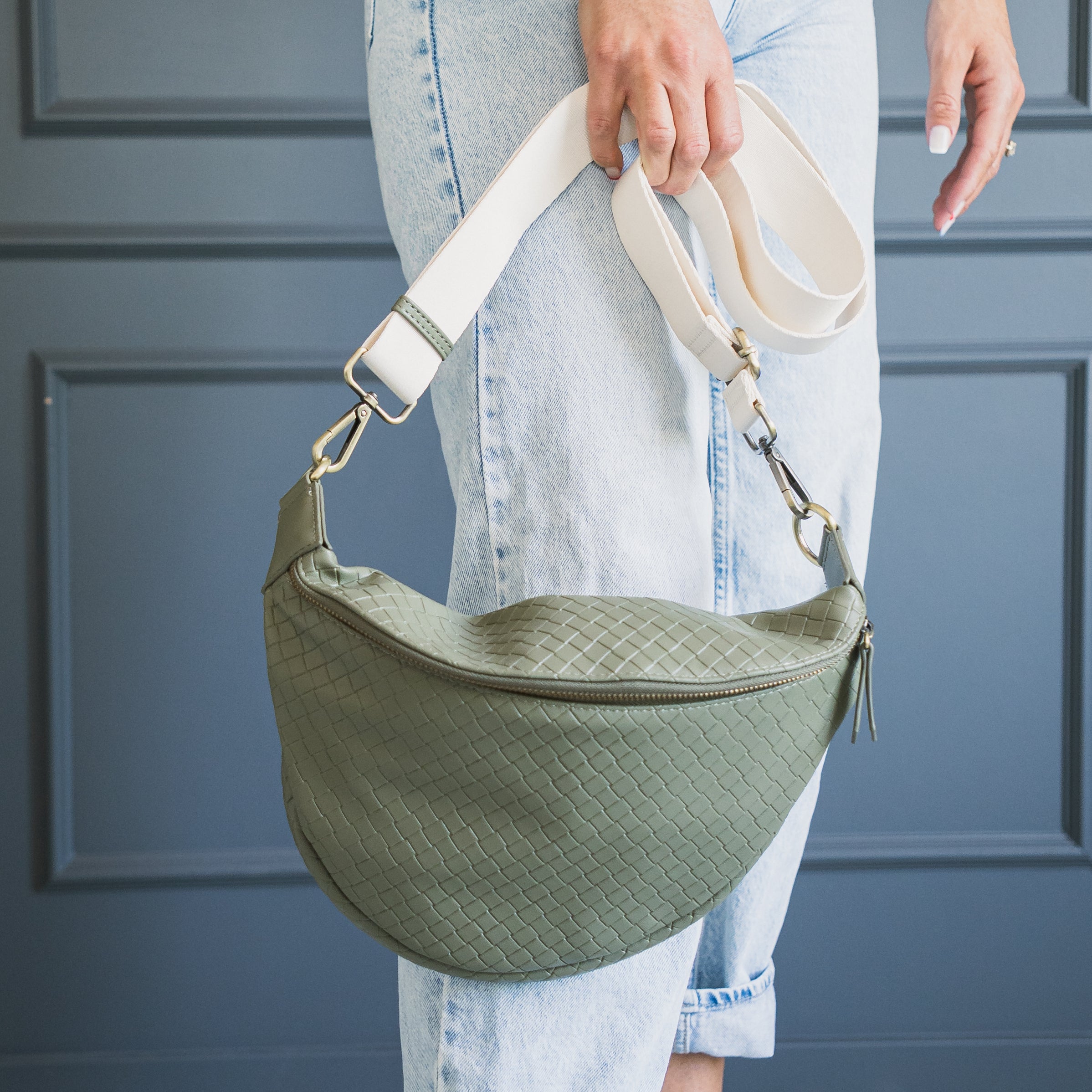Woman holding a matcha Amy crossbody bag from Pink Cove with a white strap, with a blue background.